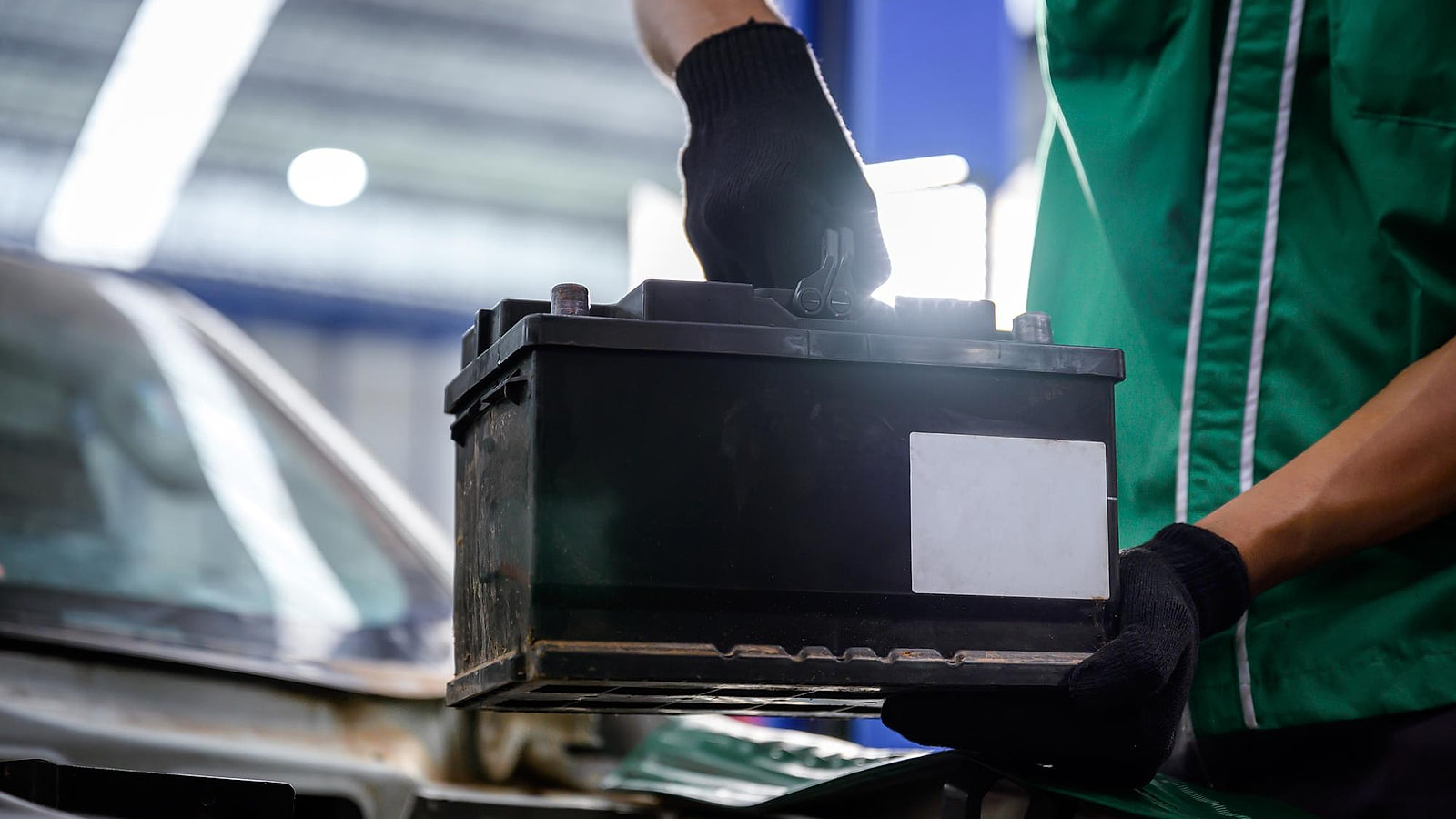Technicien en gants isolants déconnectant la batterie de traction orange d'un utilitaire électrique en atelier